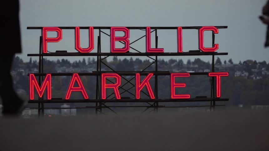 A man walks past a lit sign on a roof