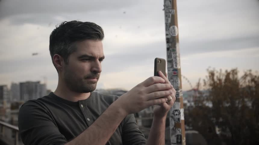 A man takes a photo with birds flying behind him