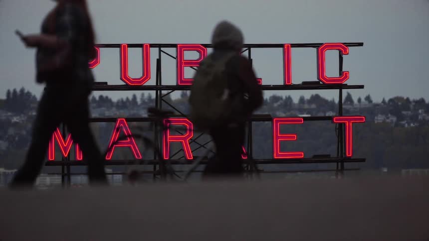 People walk past a large sign with red lit letters