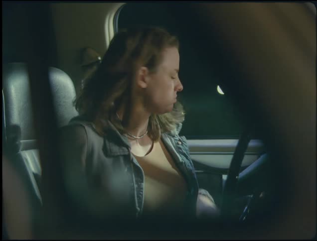 Woman with wavy hair denim jacket and brown shirt gets out of vehicle