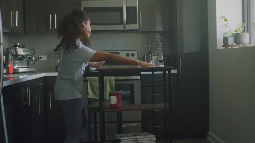 A woman gets some wipes to clean her kitchen table then makes it fun by dancing as she cleans