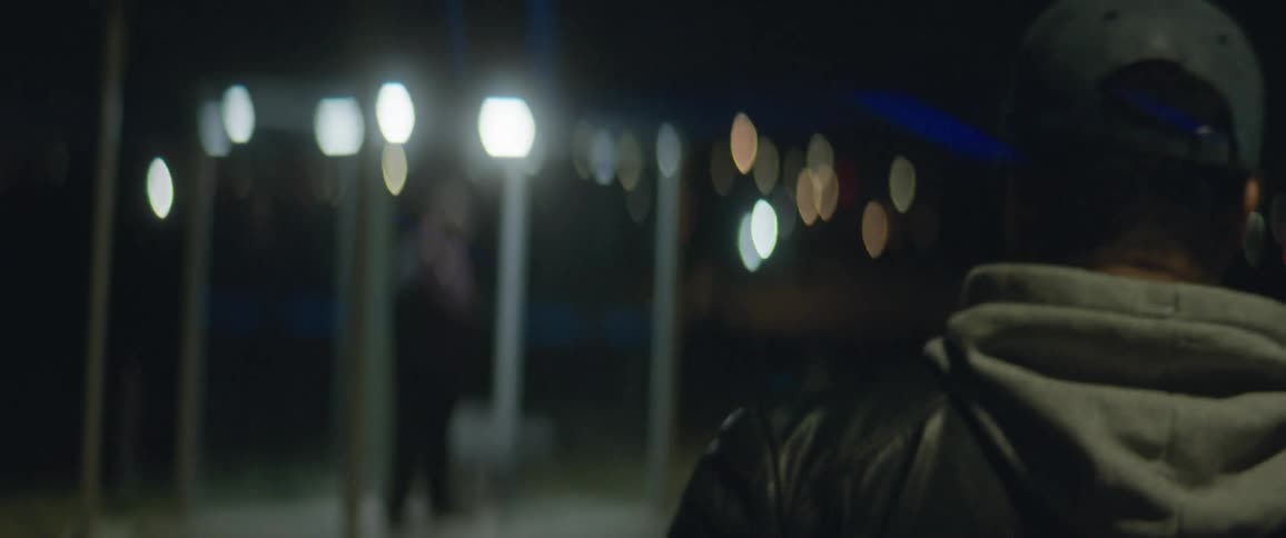 A man walks towards a bus stop where another man stands holding his cell phone