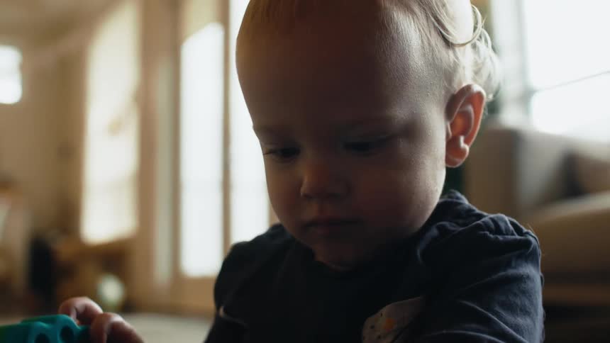 A young child sitting on the family room floor concentrating on his toys