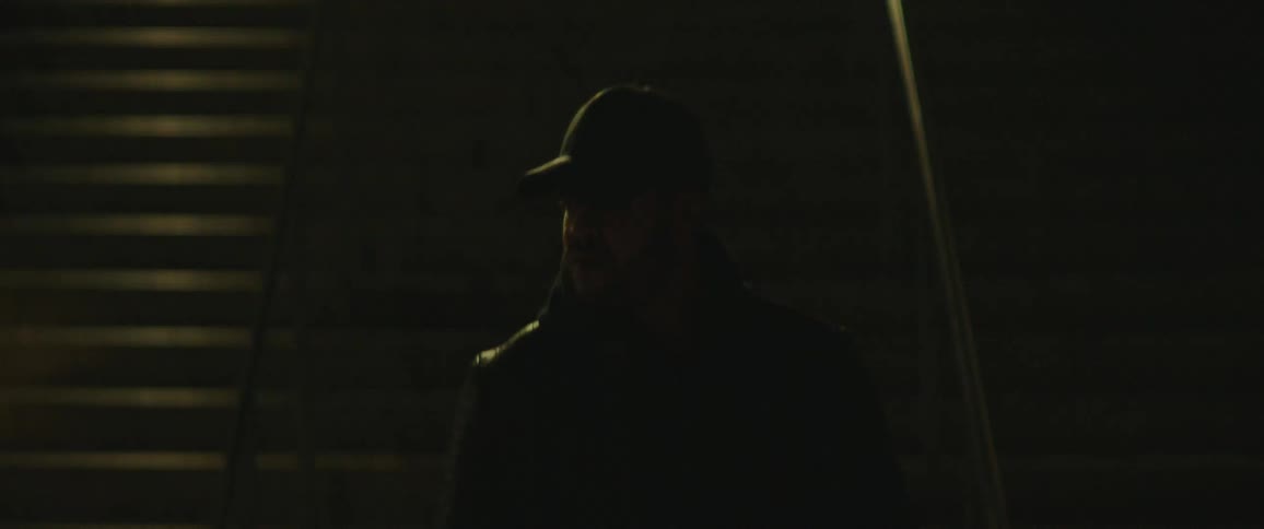 Man with cap and black jacket goes down the stairs at night