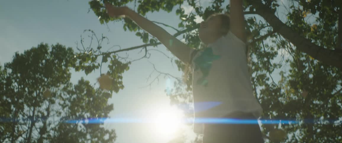 Happy girl back lit by bright sun throws leaves into the air as she jumps and spins