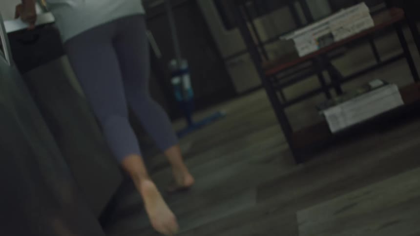 Woman with curly hair shirt and leggings mops up the kitchen dancing