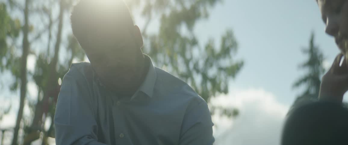 Man with beard and blue shirt sits next to woman under the shining sun