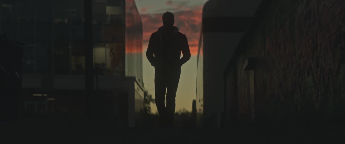 A man walks down an alley between tall apartment buildings