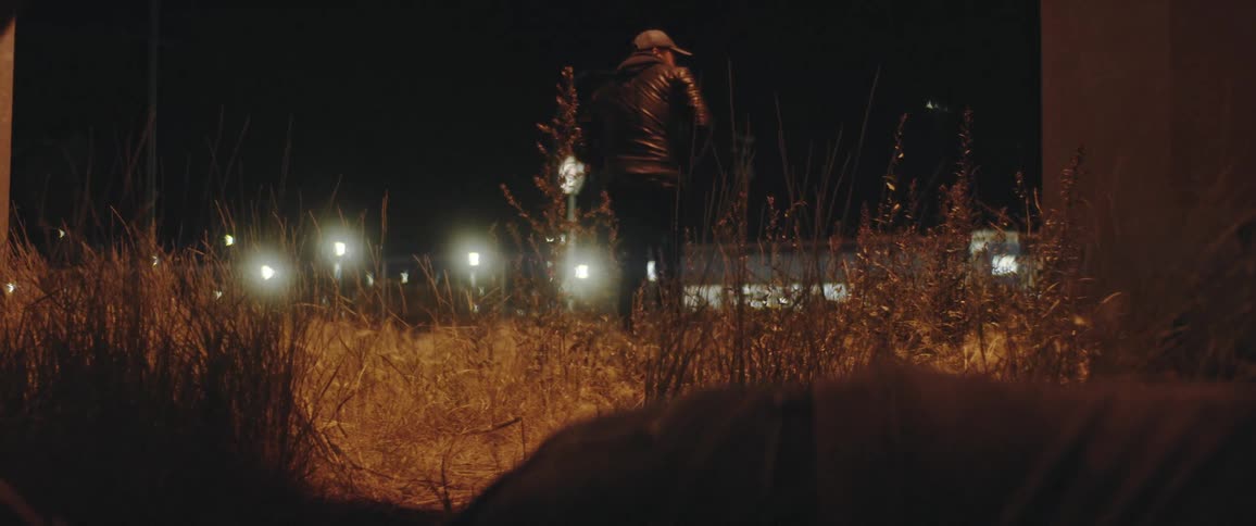 A man knocks out another man in a field as traffic passes by