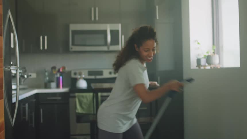 A woman is dancing while cleaning her kitchen