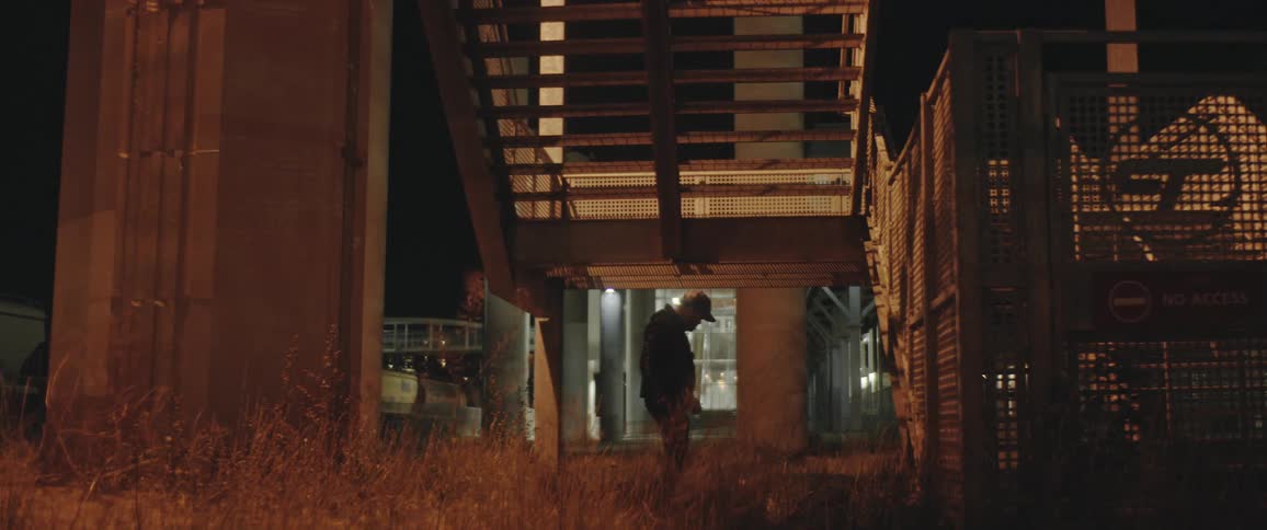A man punches another man outside a train station until he falls to the ground and then he stumbles away leaving the other man lying there
