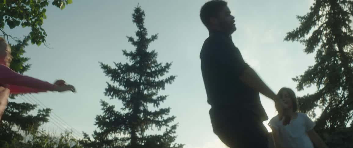 A man is out in his yard playing with his young daughter and swinging her around in the air and another girl comes to play and the man falls to the ground