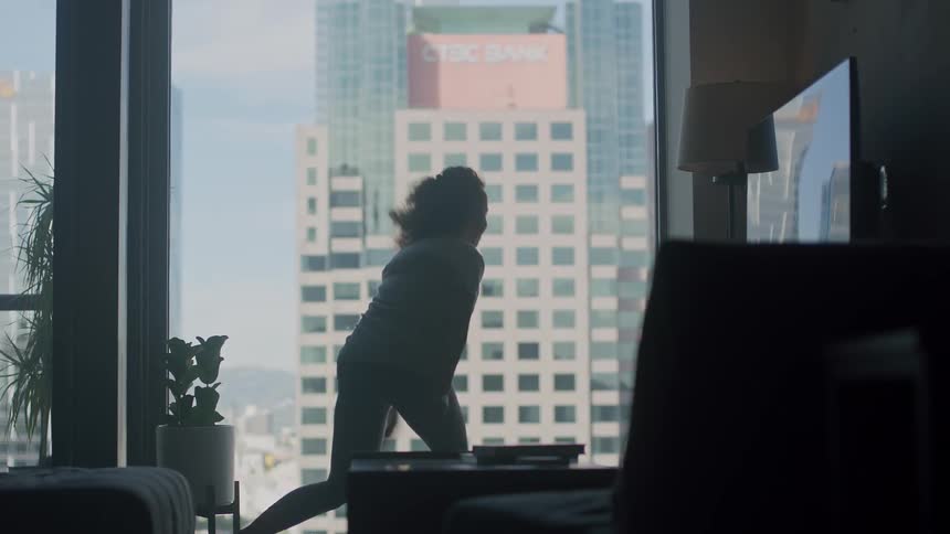 A woman is dancing near her window in a downtown city