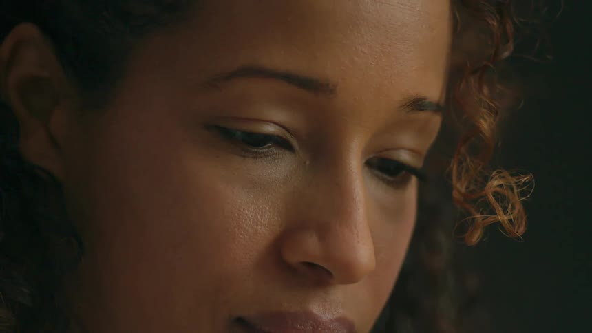 A woman with curly hair looks down with her head slightly bowed