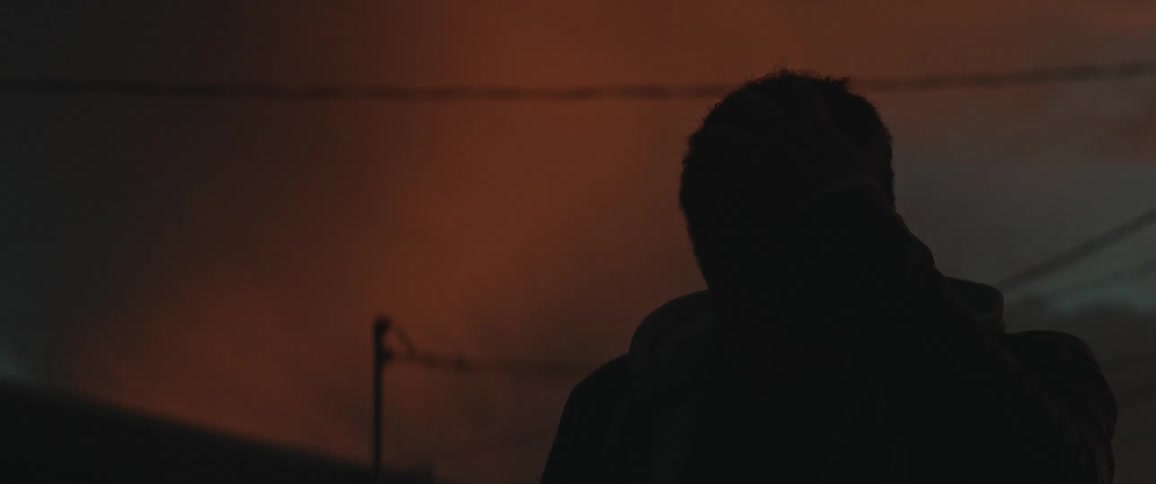 Silhouette of a man standing outside as he take off his cap and there is a red sky behind him