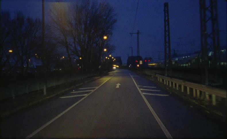 A train travels on tracks alongside a road as streetlights glow in the darkness