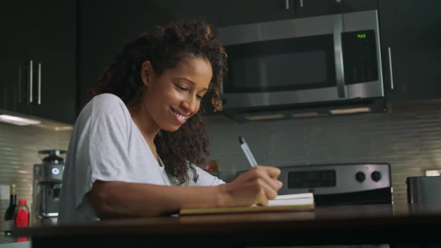 A woman smiles while writing in her kitchen