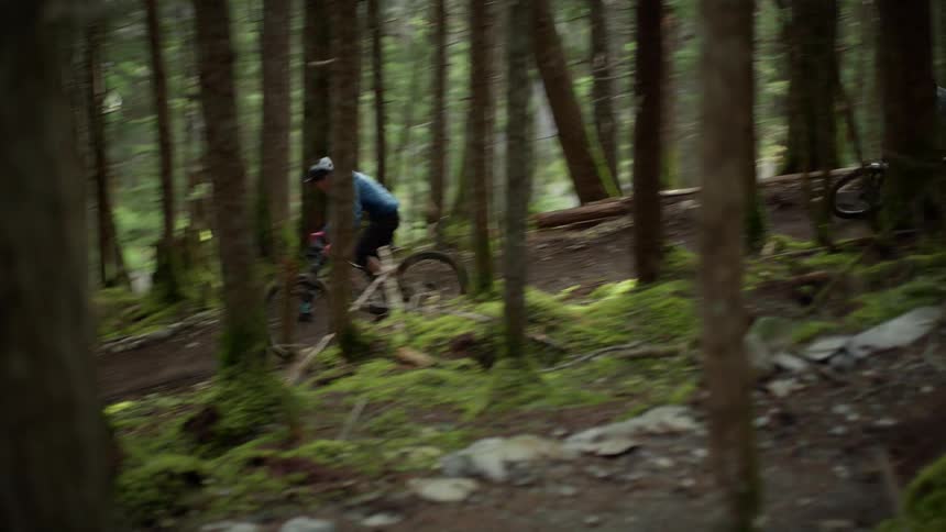 Two boys riding mountain bikes on dirt trail through the trees