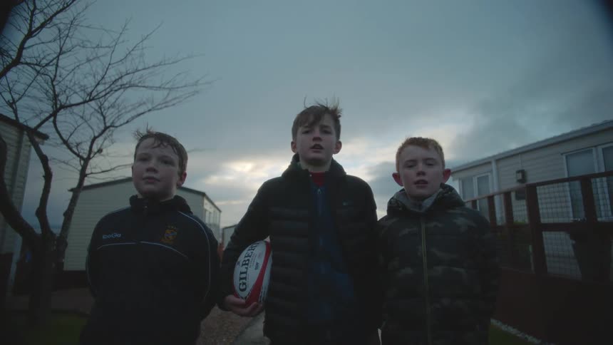 Three boys pose with ball in apartment complex under an overcast sky with a leafless tree in the background