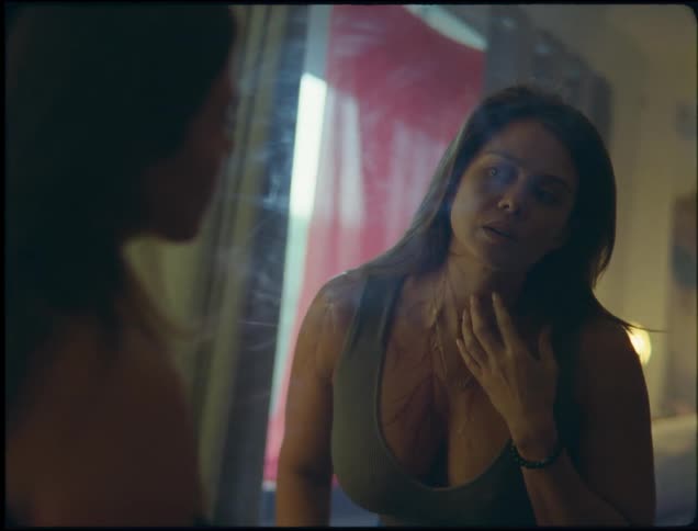 Woman stands and examines chest scars in mirror