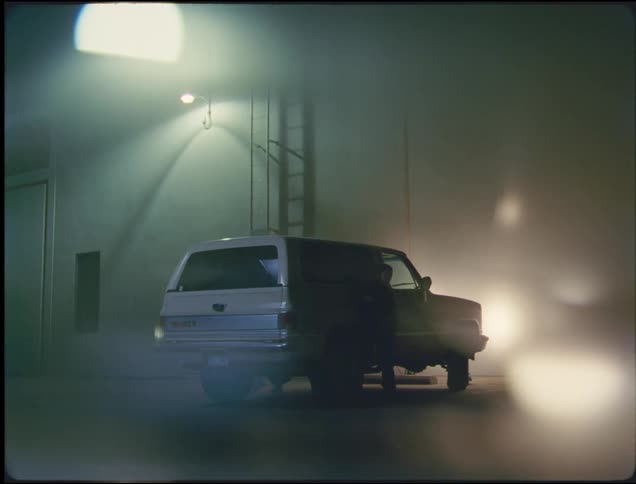 A white truck is parked outside of a building with the headlights on and two women get out
