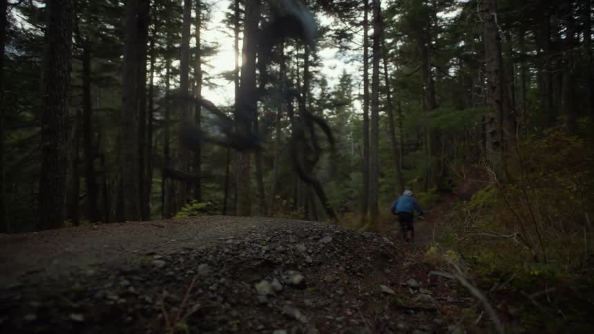 Two dirt bike riders go flying as they ride down a small hill in the woods