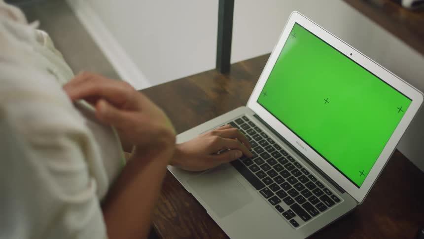 Young woman standing in front of a desk typing on her laptop