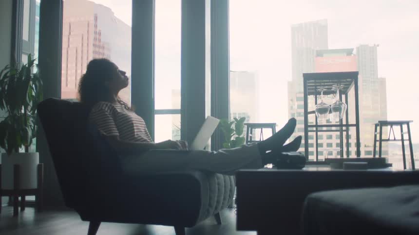 Woman with striped tshirt and jeans sits on couch using smartphone in living room at condo