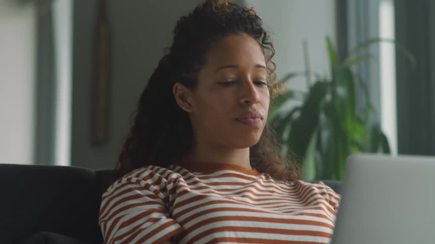 A young woman is sitting on a couch looking at a laptop
