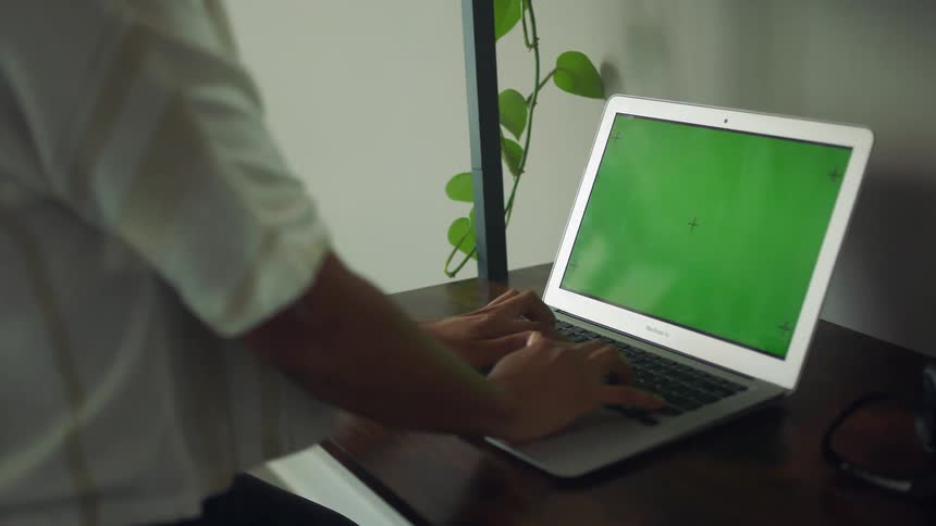 A woman typing on a laptop with a green screen