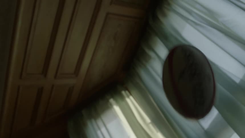 A football is being tossed into the air in a room near curtains on the windows