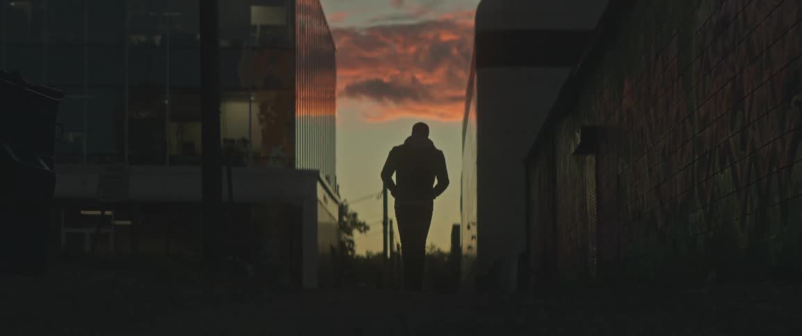 A man walks down a city sidewalk as cars drive past an office building