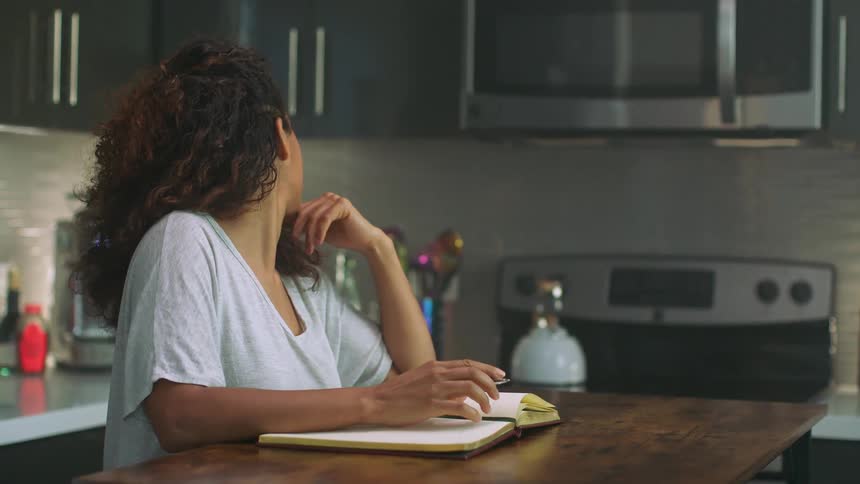 A woman gets up from writing at her kitchen table to make coffee