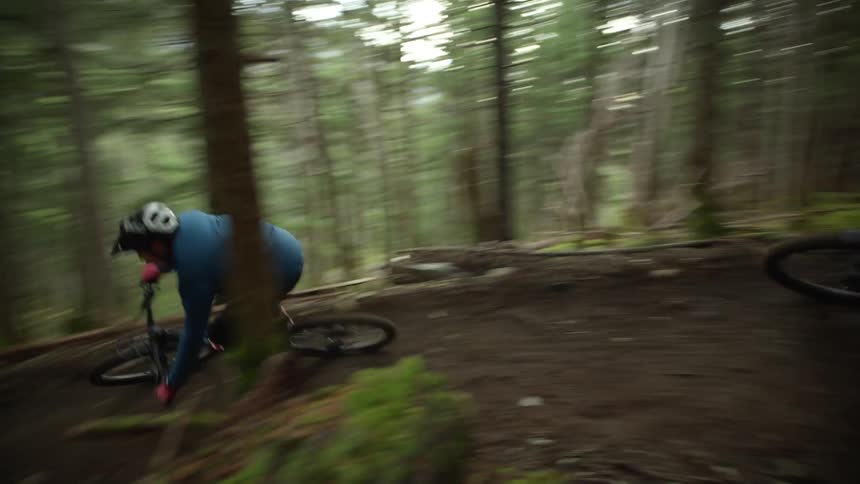 Two teenage boys mountain bike through a forest