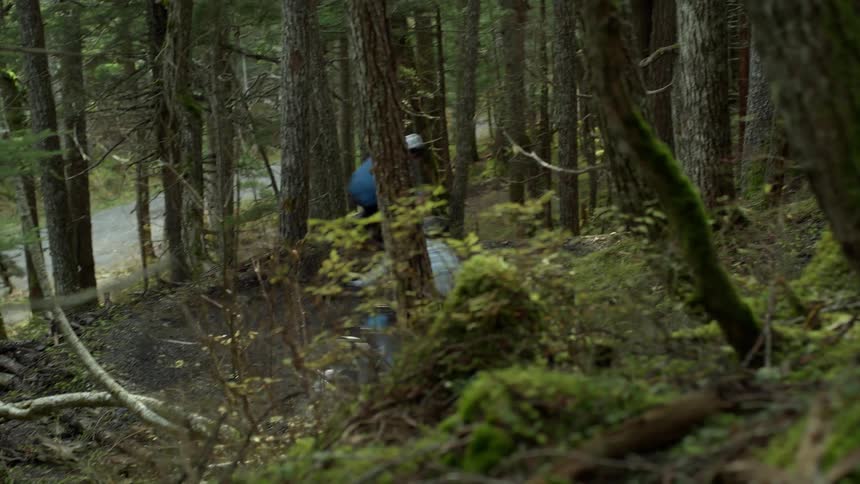 Two teenagers are dirt biking through a forest