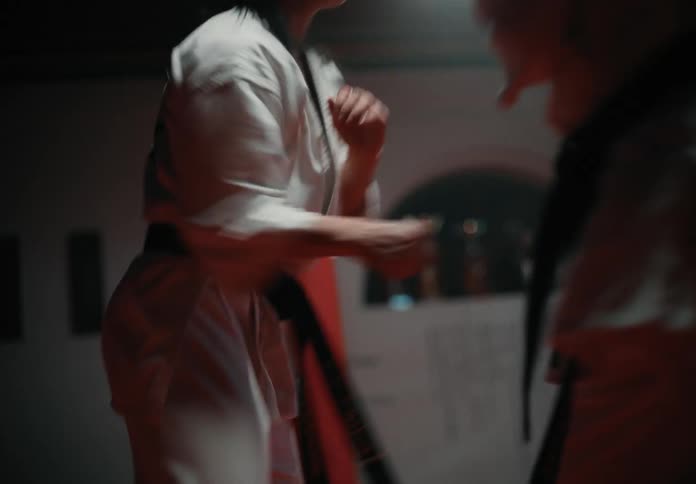 Two female martial artists wearing gi spar in dojo