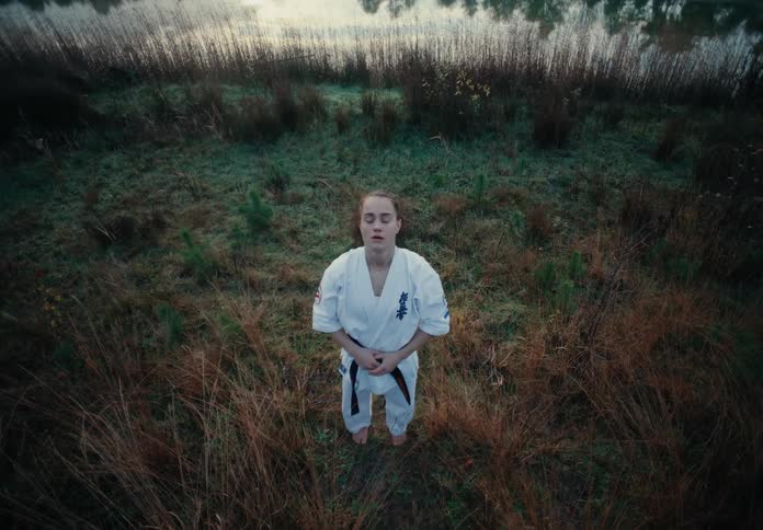 A woman standing barefoot in the grass wearing a karate gi taking a deep breath to center herself
