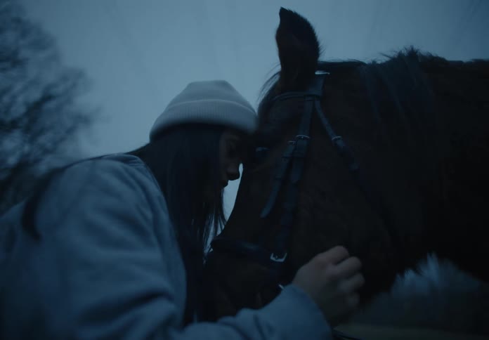 A woman wearing a coat and a white knit cap is outside petting her horses face and head in a very loving manner