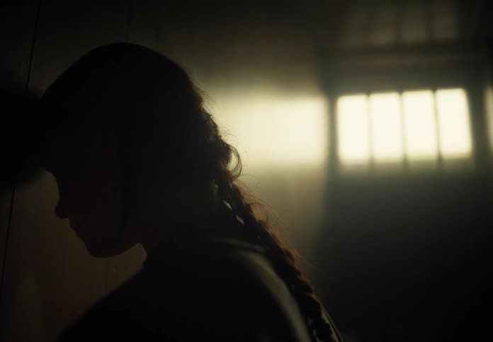 A young woman leans her head against the wall inside a darkly lit room