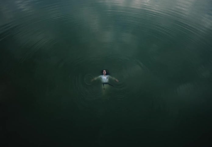 A high shot looking down at a young woman in martial arts attire floating in the middle of a lake