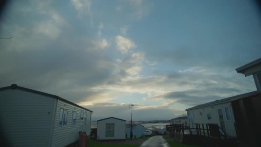 Mobile homes sits on either side of paved road cutting through mobile home park under a cloudy sky