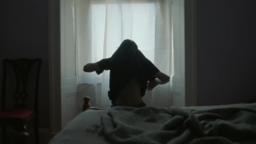 A child puts on his shirt in the bedroom
