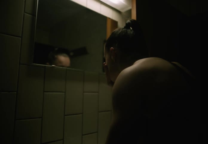 A woman is leaning over a sink looking in the mirror and splashing water on her face