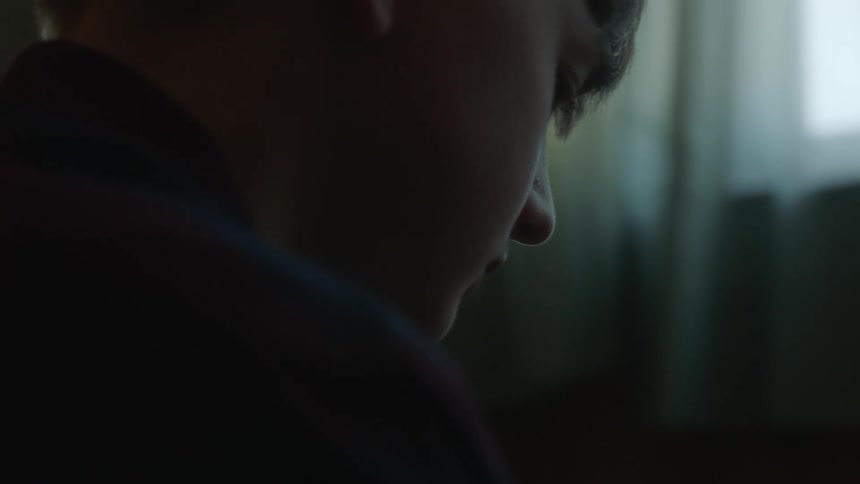 A young boy sits and looks at a football as he turns it in his hands