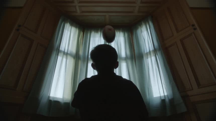 A child throws a football while sitting by the window