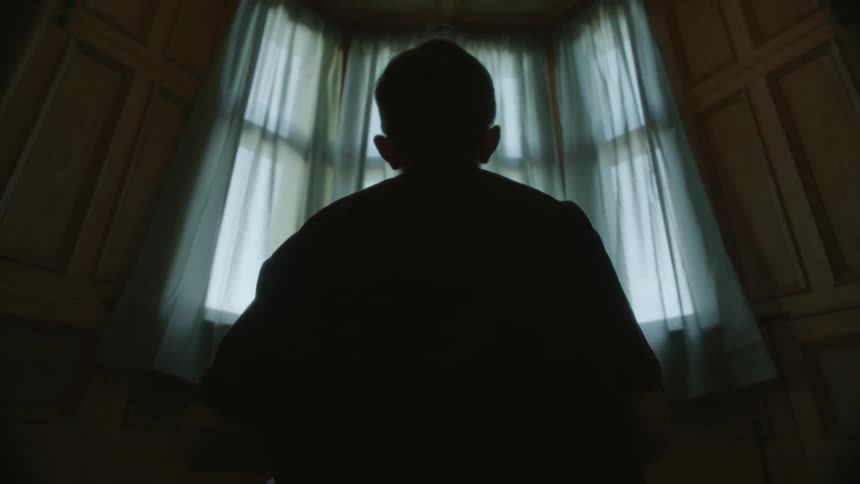 A boy is sitting in a room near a window