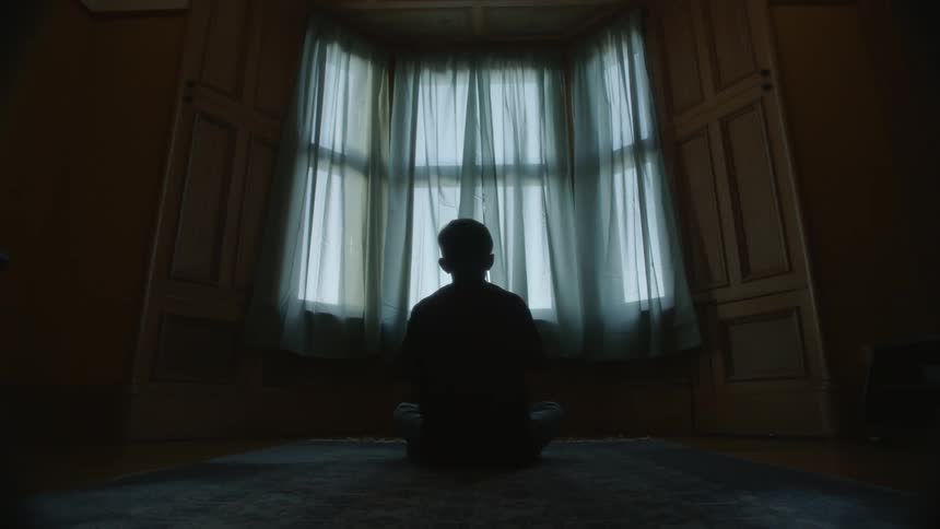 A boy is sitting on the floor tossing a football into the air and catching it
