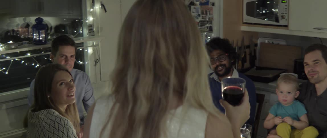 Happy blonde woman standing to give a celebratory toast at a social dinner gathering.