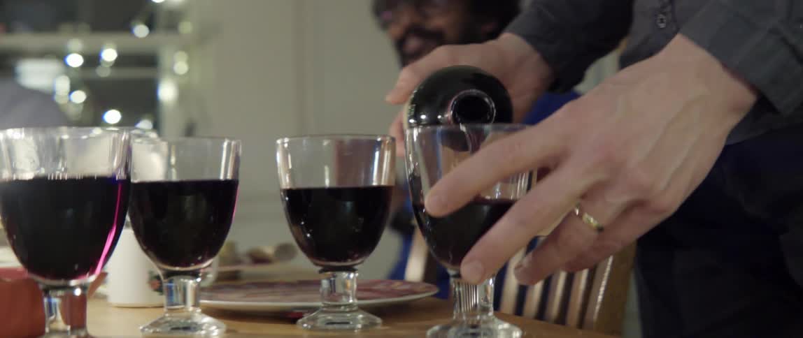 Person serving red wine to friends seated around a modern dining table at home.