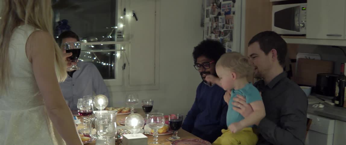 A woman holding a glass of wine talks to a table of people in a home